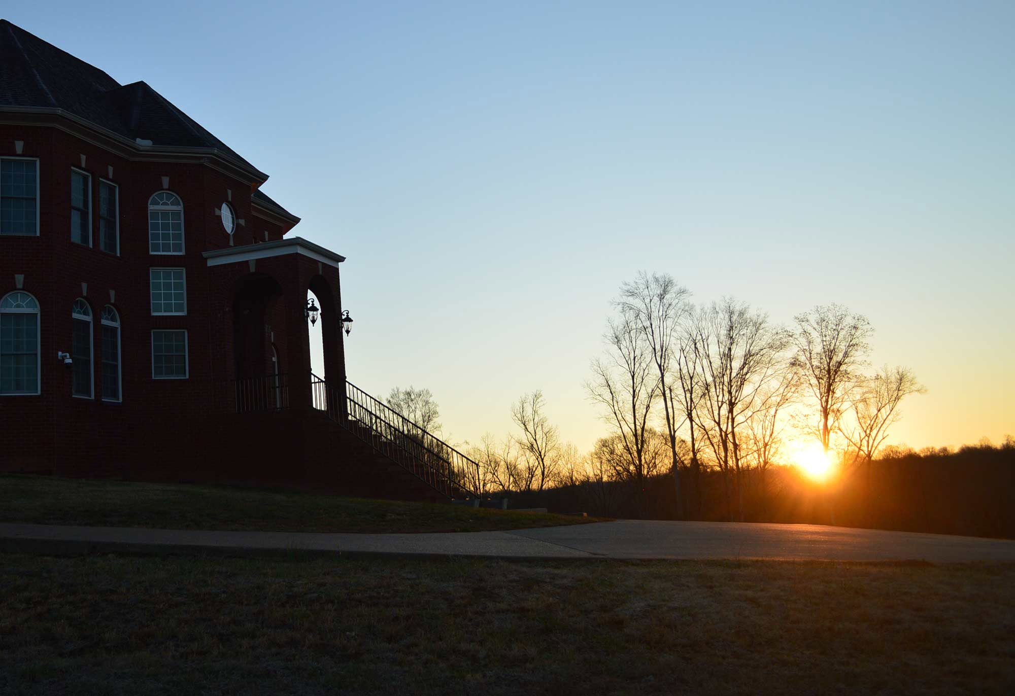 sun rising behind the trees with the Magnolia Meadows home in the foreground